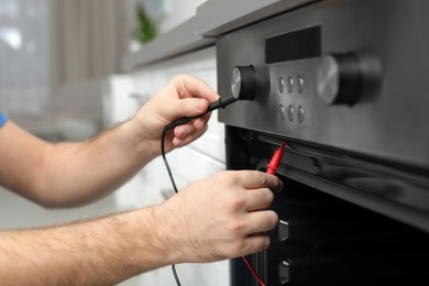 Photo of Professional serviceman repairing modern oven in kitchen, closeup