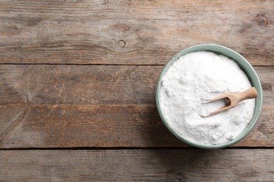 Photo of Bowl with baking soda and scoop on wooden table, top view