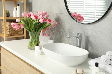 Photo of Vase with beautiful pink tulips and toiletries near sink in bathroom