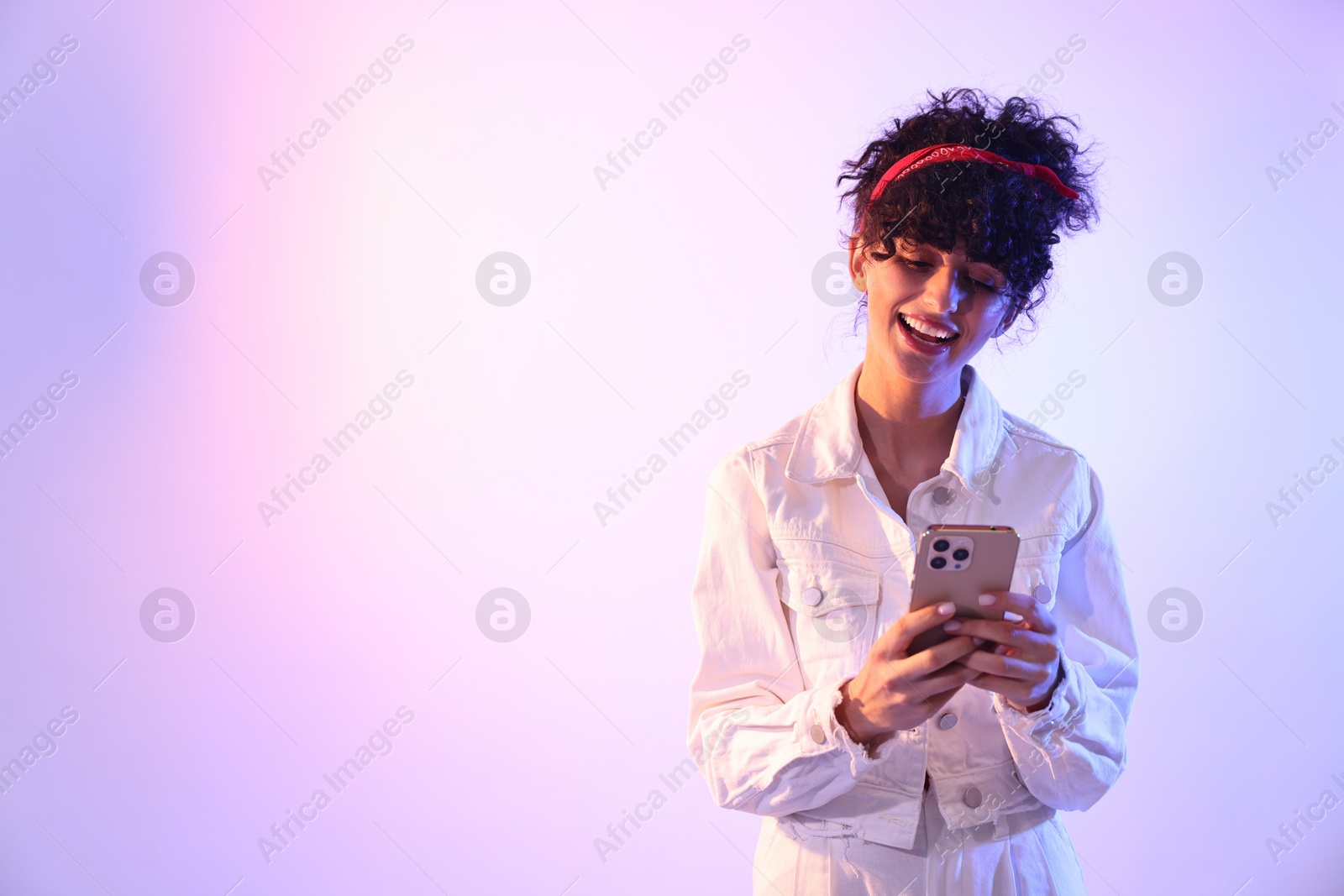 Photo of Beautiful young woman with smartphone against color background in neon lights. Space for text