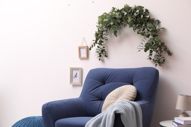 Photo of Beautiful garland made of eucalyptus branches hanging above armchair on white wall indoors