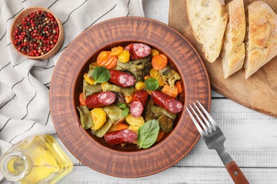 Photo of Delicious sausage and baked vegetables served on white wooden table, flat lay