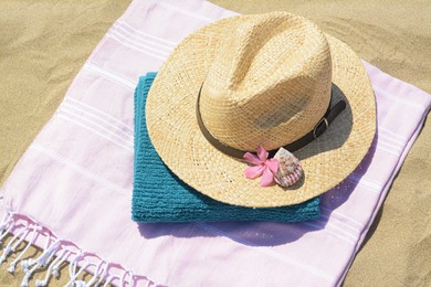 Photo of Blanket with towel, stylish straw hat and flower on sand outdoors, above view. Beach accessories