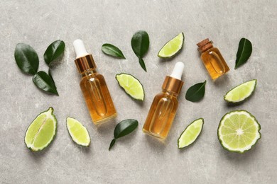 Photo of Glass bottles of bergamot essential oil and fresh fruits on light grey table, flat lay