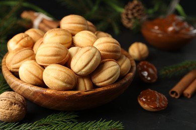 Photo of Homemade walnut shaped cookies with boiled condensed milk, cinnamon sticks and fir branches on black table