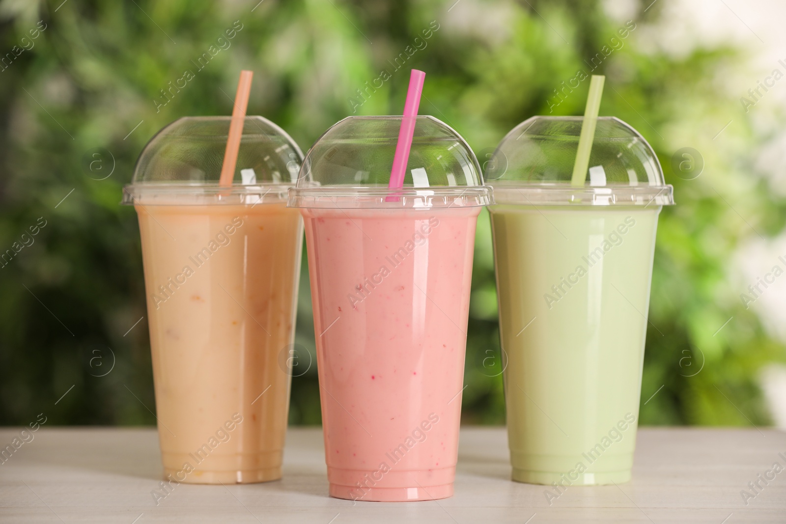 Photo of Plastic cups with different tasty smoothies on wooden table outdoors