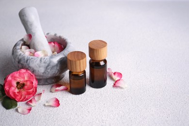 Photo of Glass bottles of aromatic essential oil, mortar with roses on white table, space for text
