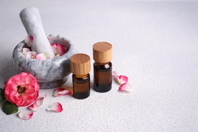 Glass bottles of aromatic essential oil, mortar with roses on white table, space for text