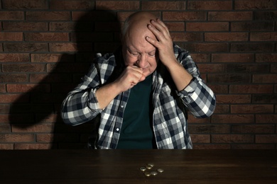Photo of Poor senior man with coins at table near brick wall