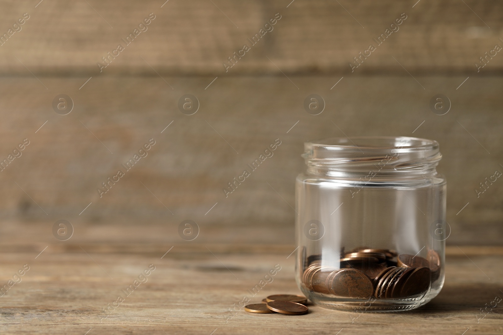 Photo of Glass jar with coins on wooden table. Space for text