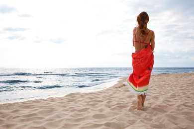 Woman with bright beach towel on seashore, back view