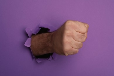 Photo of Man breaking through purple paper with fist, closeup