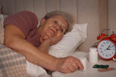 Photo of Elderly woman suffering from insomnia taking pill bottle in bed at night