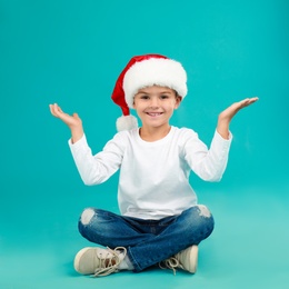 Photo of Cute little child wearing Santa hat on light blue background. Christmas holiday