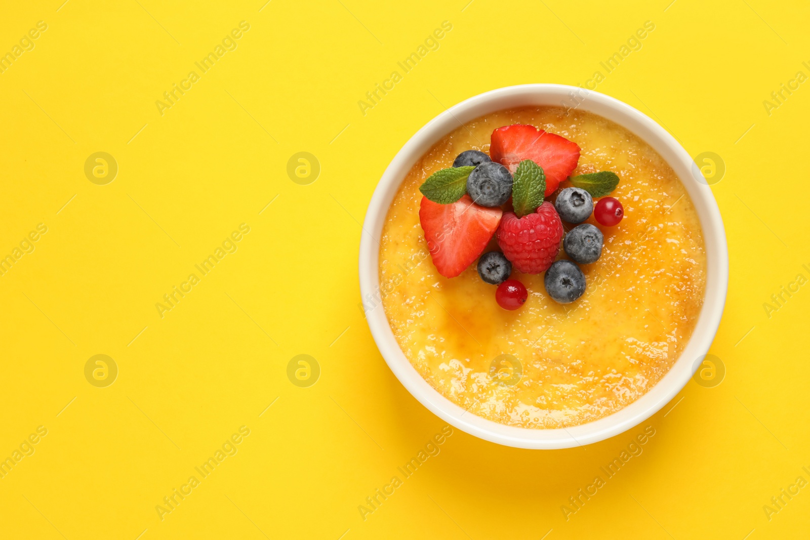 Photo of Delicious creme brulee with fresh berries on yellow background, top view. Space for text