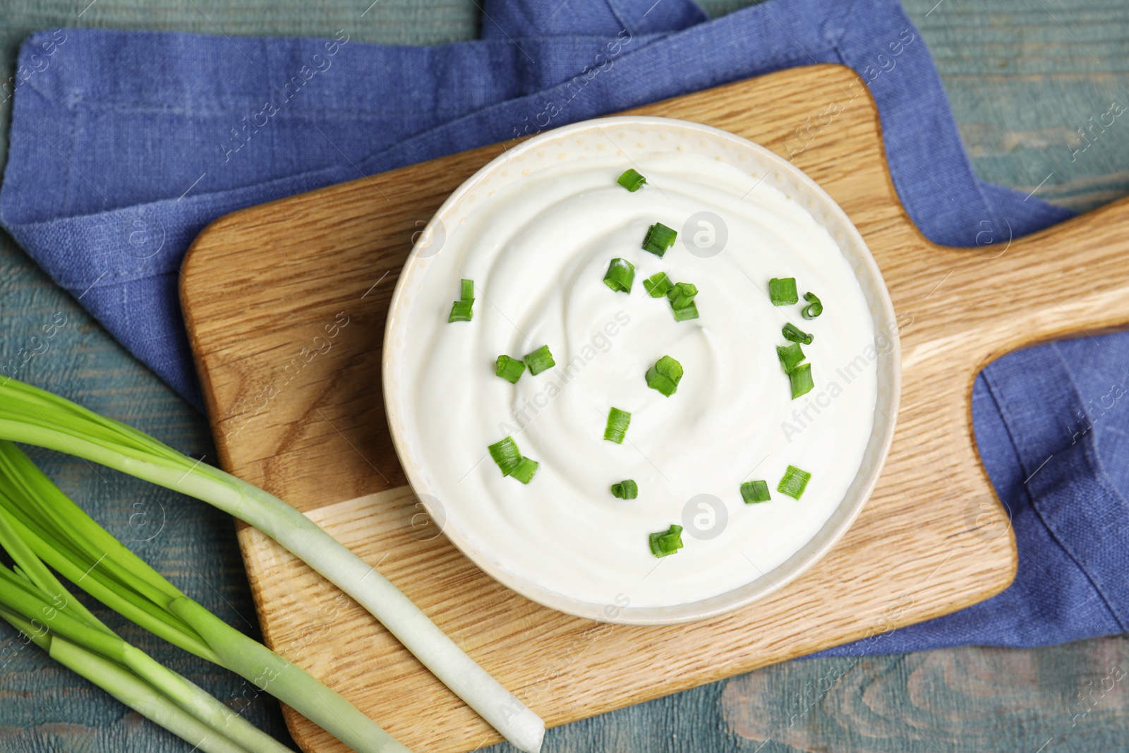 Photo of Fresh sour cream with onion on light blue wooden table, flat lay