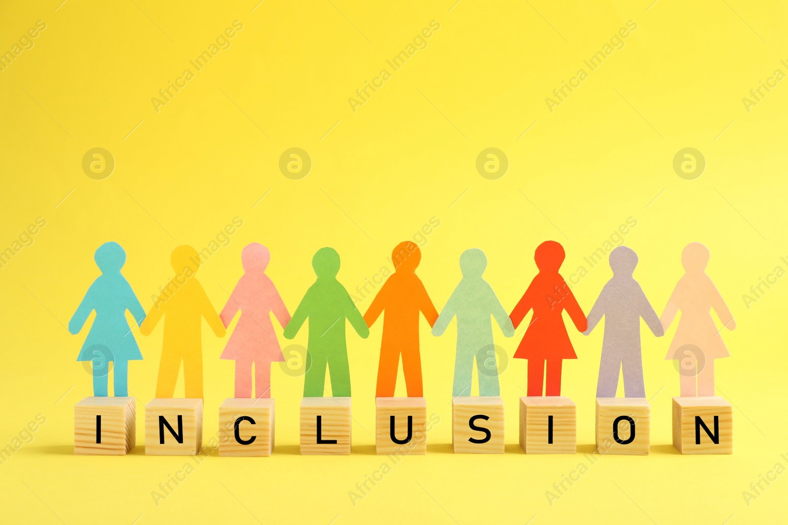 Photo of Paper human figures and wooden cubes with word Inclusion on yellow background