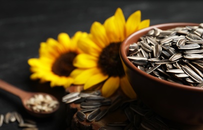 Photo of Raw sunflower seeds and flowers on black table, closeup. Space for text