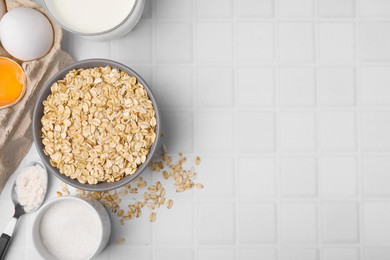 Photo of Different ingredients for cooking tasty oatmeal pancakes on white tiled table, flat lay. Space for text