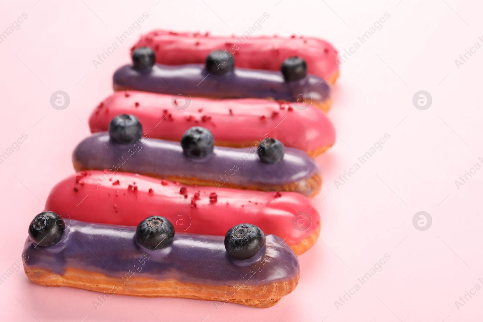 Photo of Delicious eclairs covered with glaze on pink background, closeup