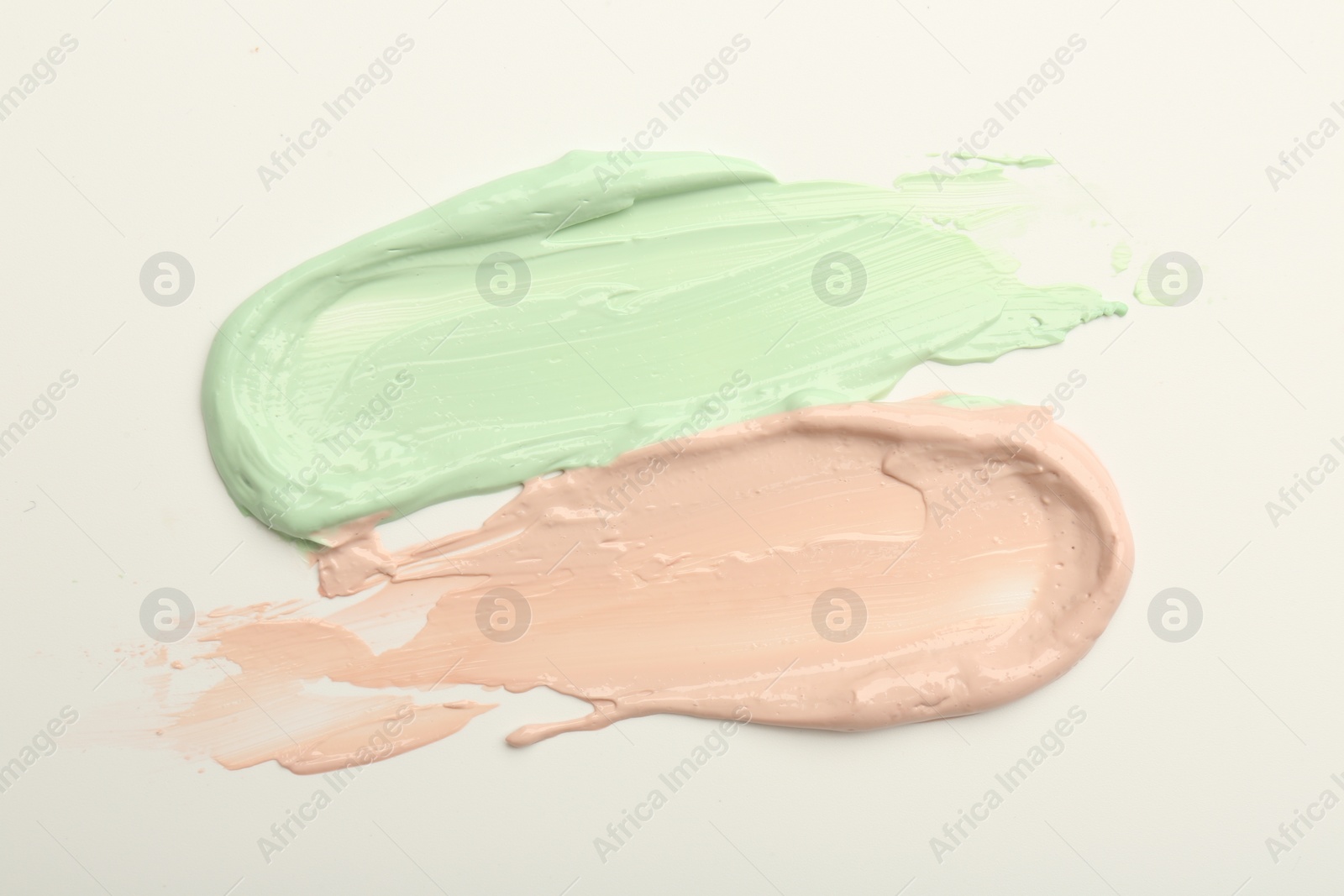 Photo of Strokes of pink and green color correcting concealers on white background, top view