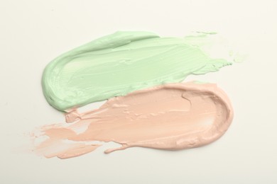 Photo of Strokes of pink and green color correcting concealers on white background, top view
