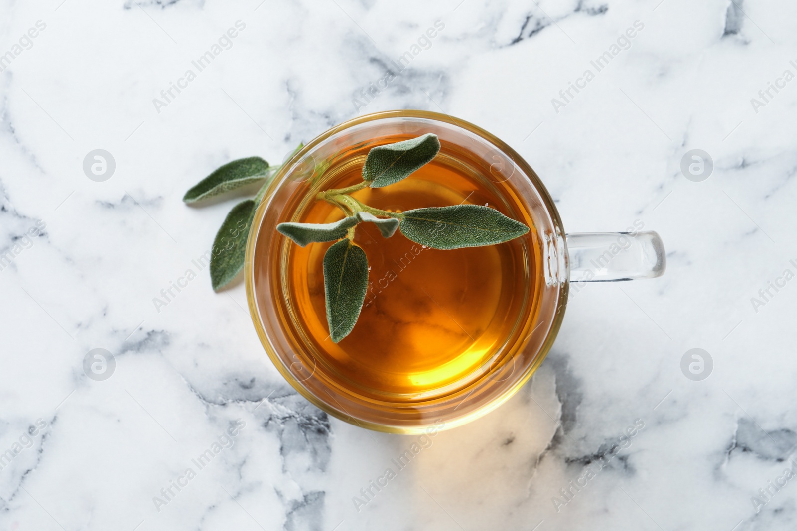 Photo of Cup of aromatic sage tea with fresh leaves on white marble table, top view