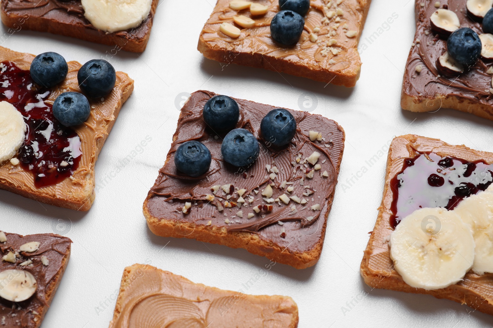 Photo of Different tasty toasts with nut butter and products on white table, closeup