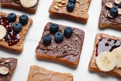 Different tasty toasts with nut butter and products on white table, closeup
