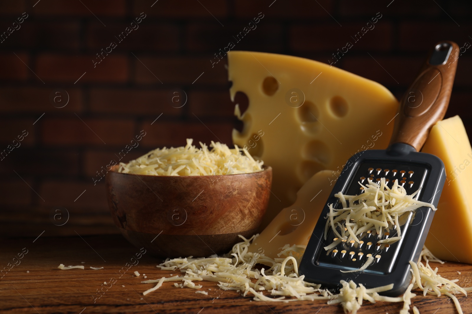 Photo of Grated, cut cheese and grater on wooden board, closeup