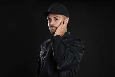 Photo of Male security guard in uniform using radio earpiece on dark background