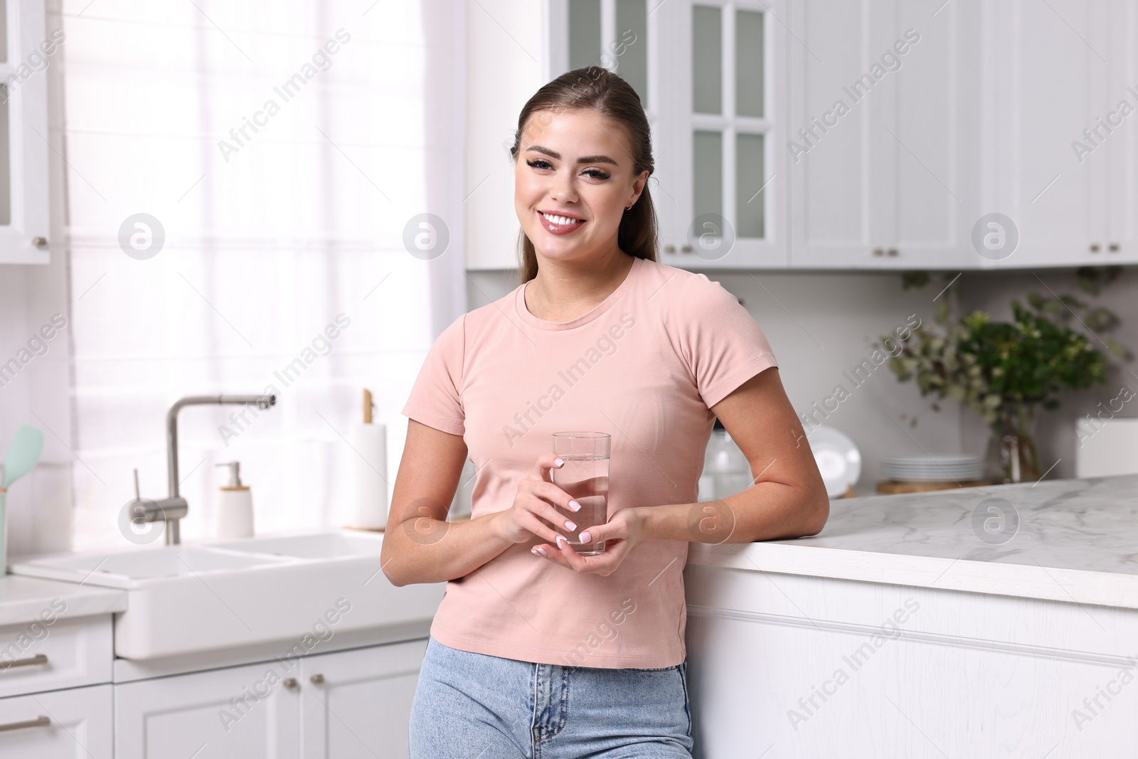 Photo of Happy woman with glass of fresh water in kitchen