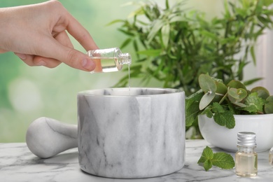 Woman pouring essential oil into mortar on table