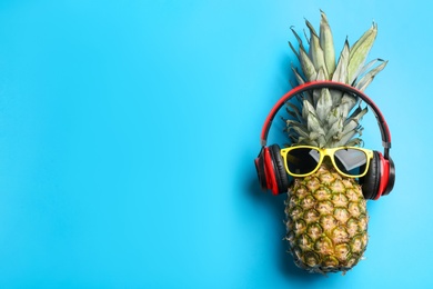 Photo of Top view of pineapple with headphones and sunglasses on light blue background, space for text. Creative concept
