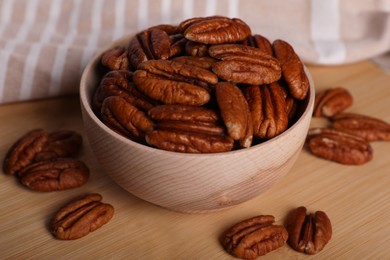 Tasty pecan nuts with bowl on wooden table, closeup