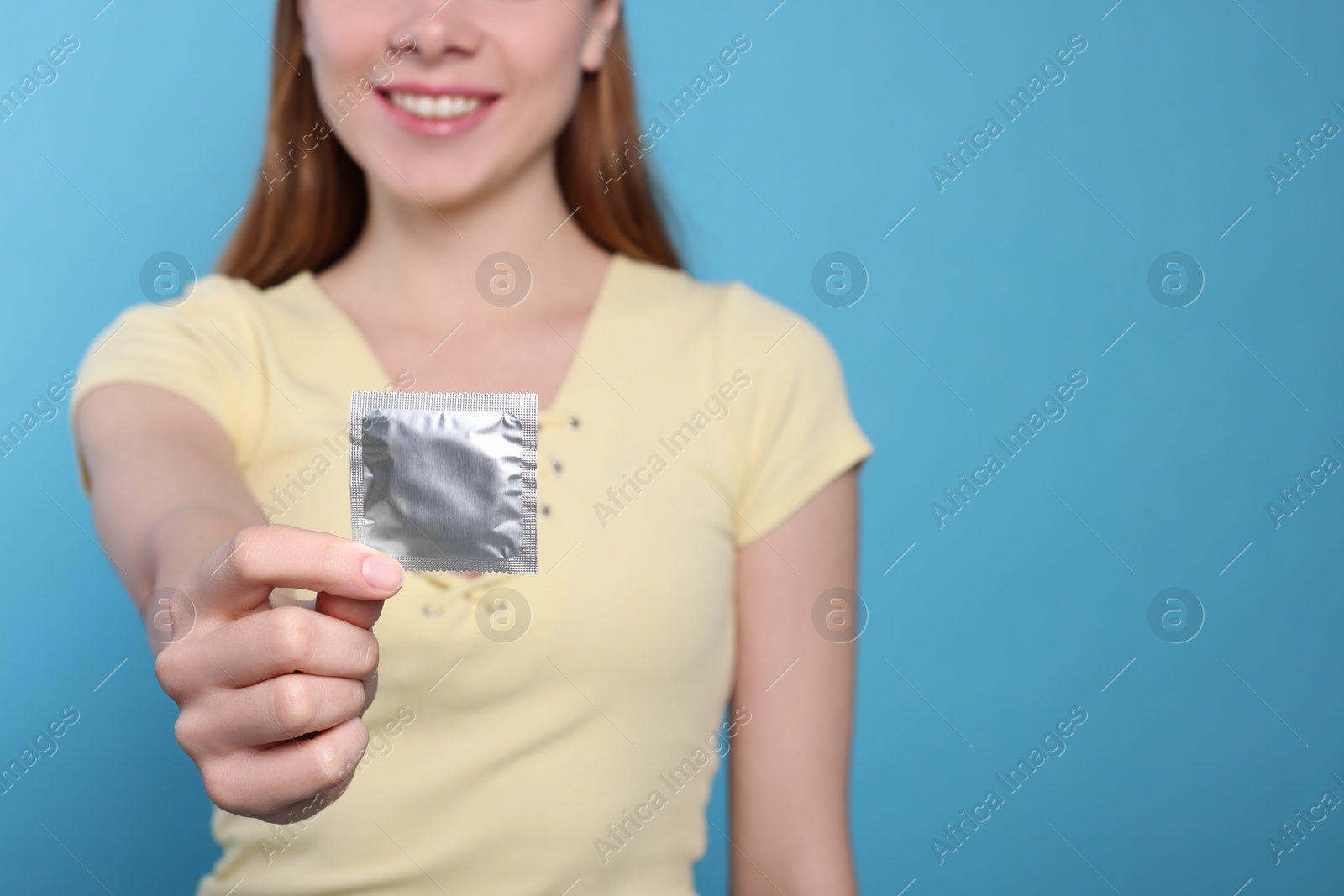 Photo of Woman holding condom on turquoise background, closeup and space for text. Safe sex