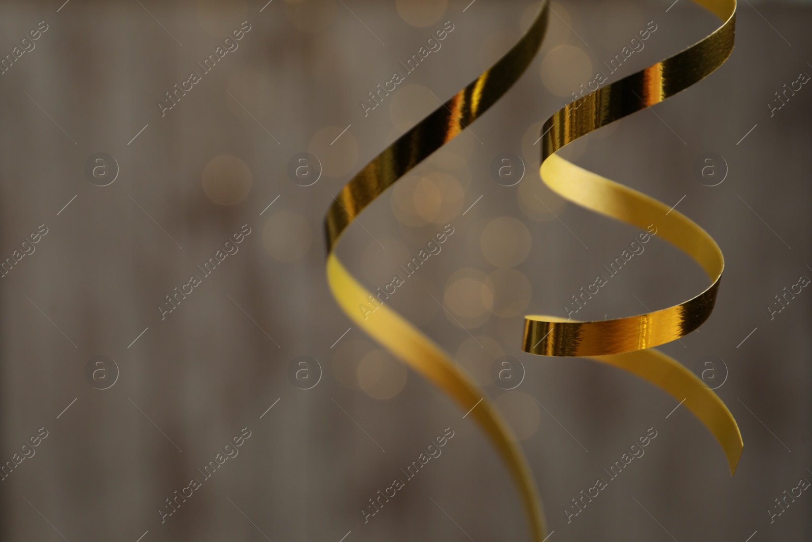 Photo of Shiny golden serpentine streamers against blurred lights, closeup. Space for text