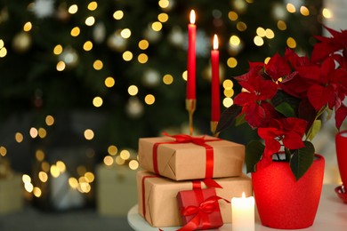 Photo of Potted poinsettias, burning candles and festive decor on white table in room, space for text. Christmas traditional flower