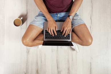 Young man with laptop sitting on floor, top view