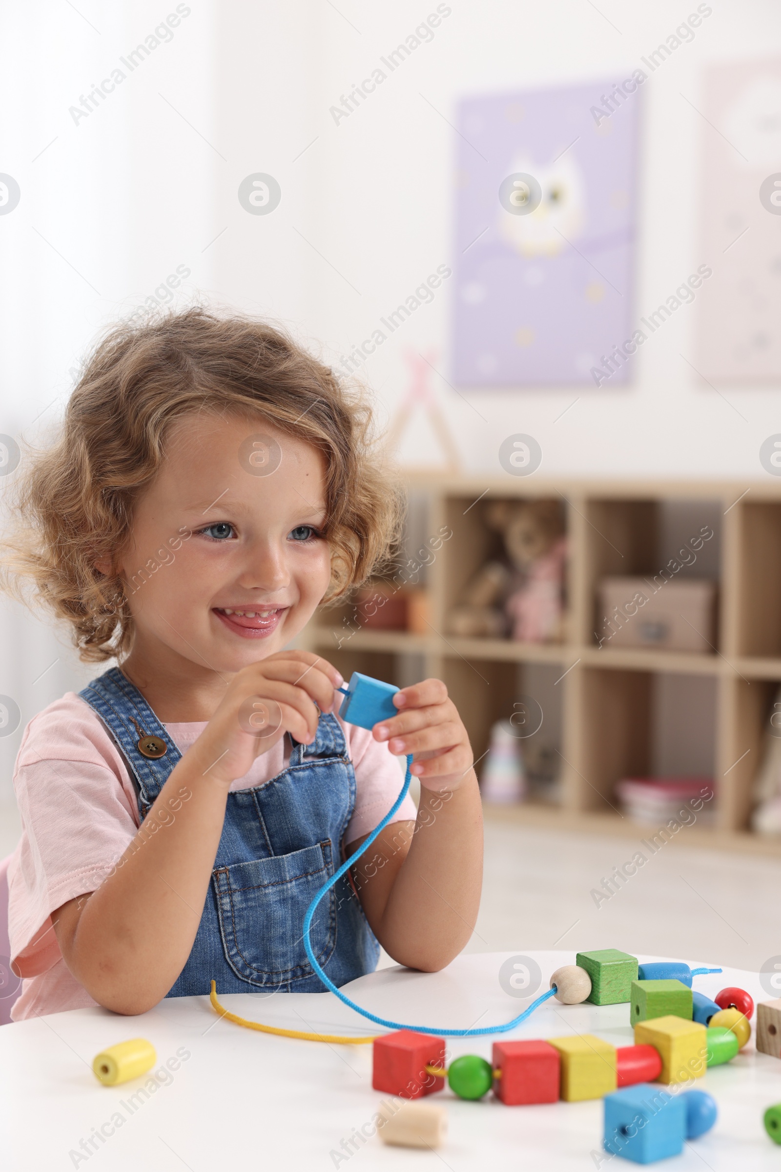 Photo of Motor skills development. Little girl playing with wooden pieces and string for threading activity at table indoors