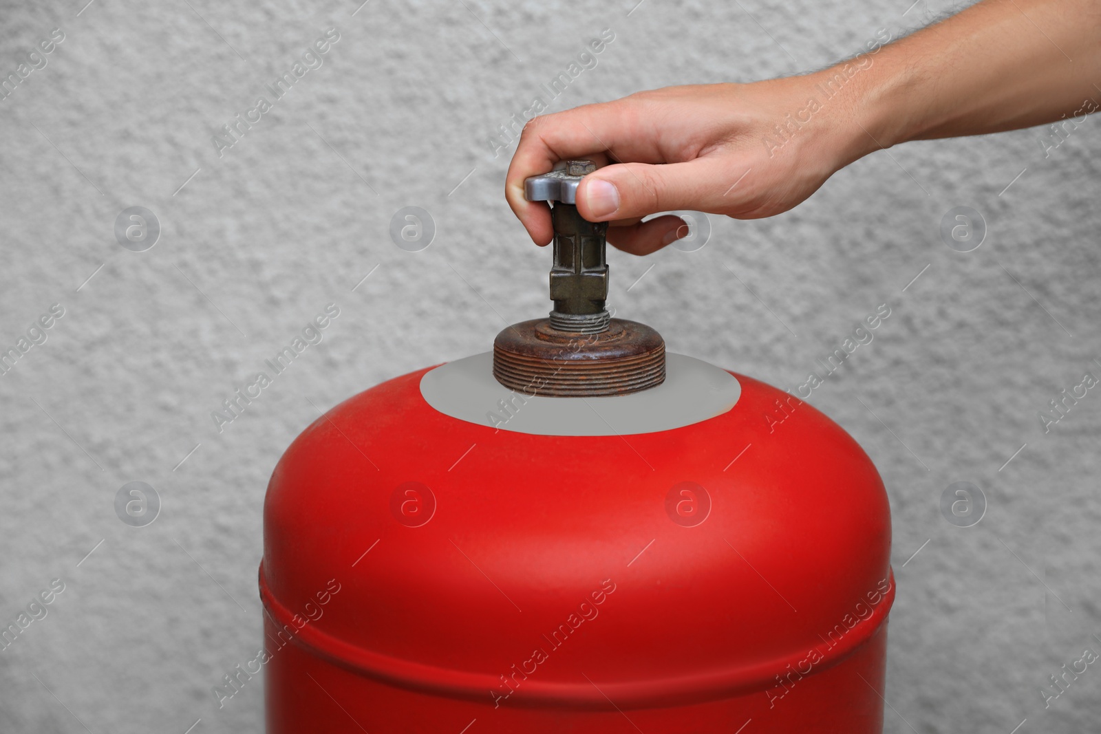 Photo of Man opening red gas cylinder near wall, closeup