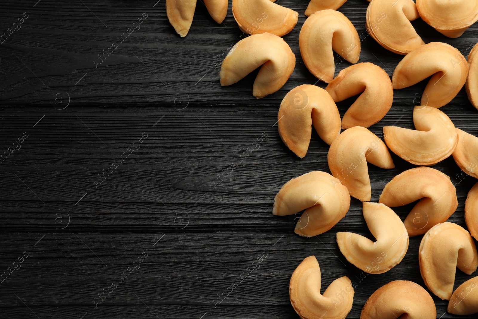 Photo of Tasty fortune cookies with predictions on black wooden table, flat lay. Space for text