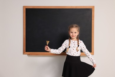 Photo of Pupil with school bell near black chalkboard in classroom