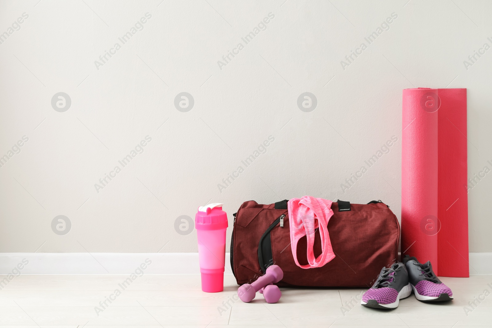 Photo of Red bag and sports accessories on floor near light wall, space for text