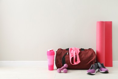 Red bag and sports accessories on floor near light wall, space for text