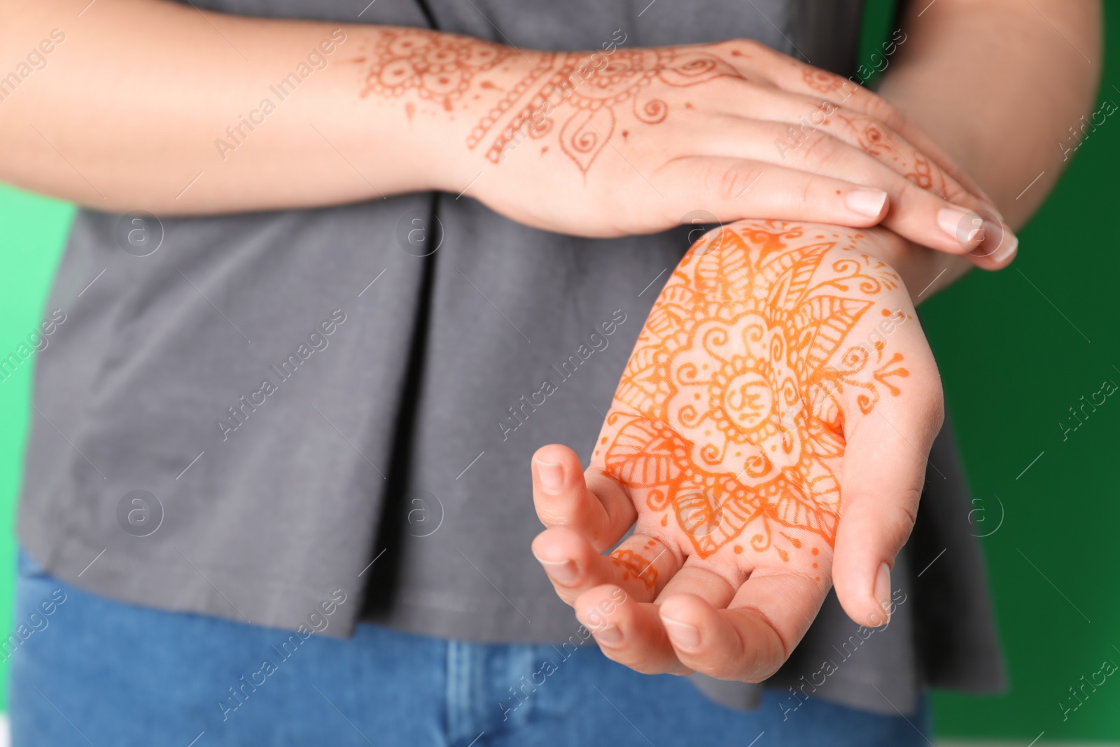 Photo of Woman with henna tattoos on hands against green background, closeup. Traditional mehndi ornament