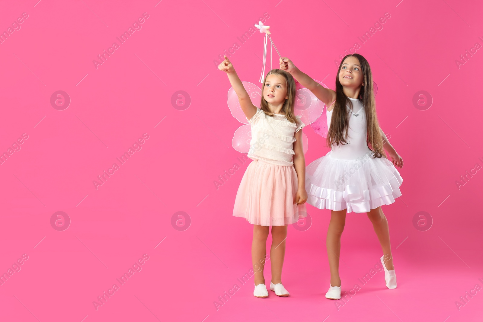 Photo of Cute little girls in fairy costumes with wings and magic wand on pink background. Space for text
