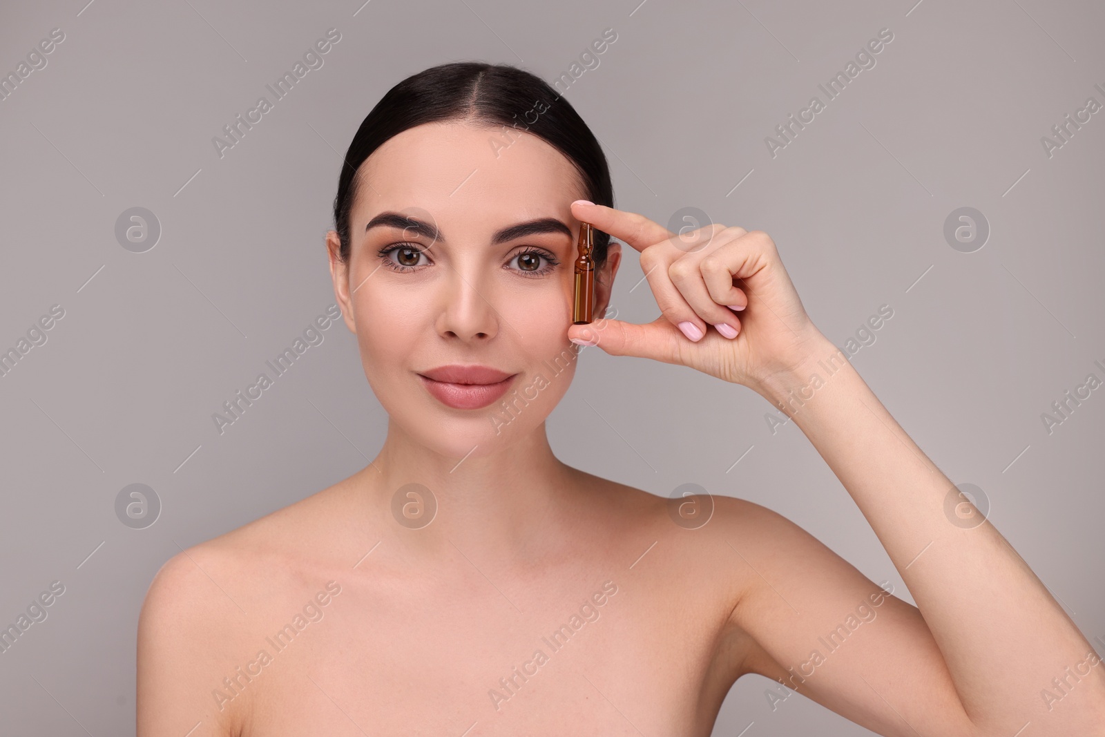 Photo of Beautiful young woman holding skincare ampoule on grey background