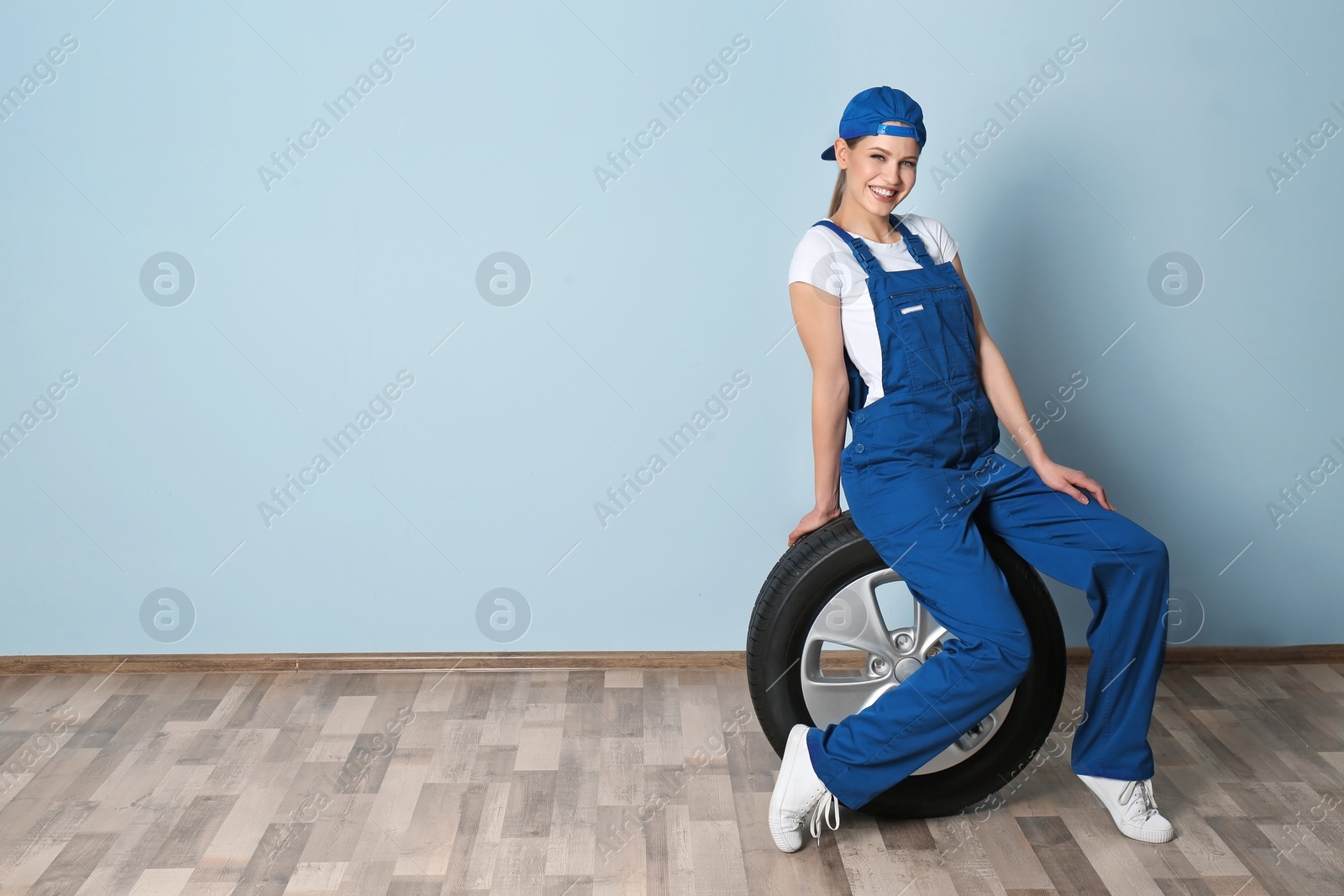 Photo of Female mechanic with car tire on grey wall background