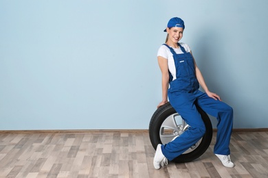 Female mechanic with car tire on grey wall background